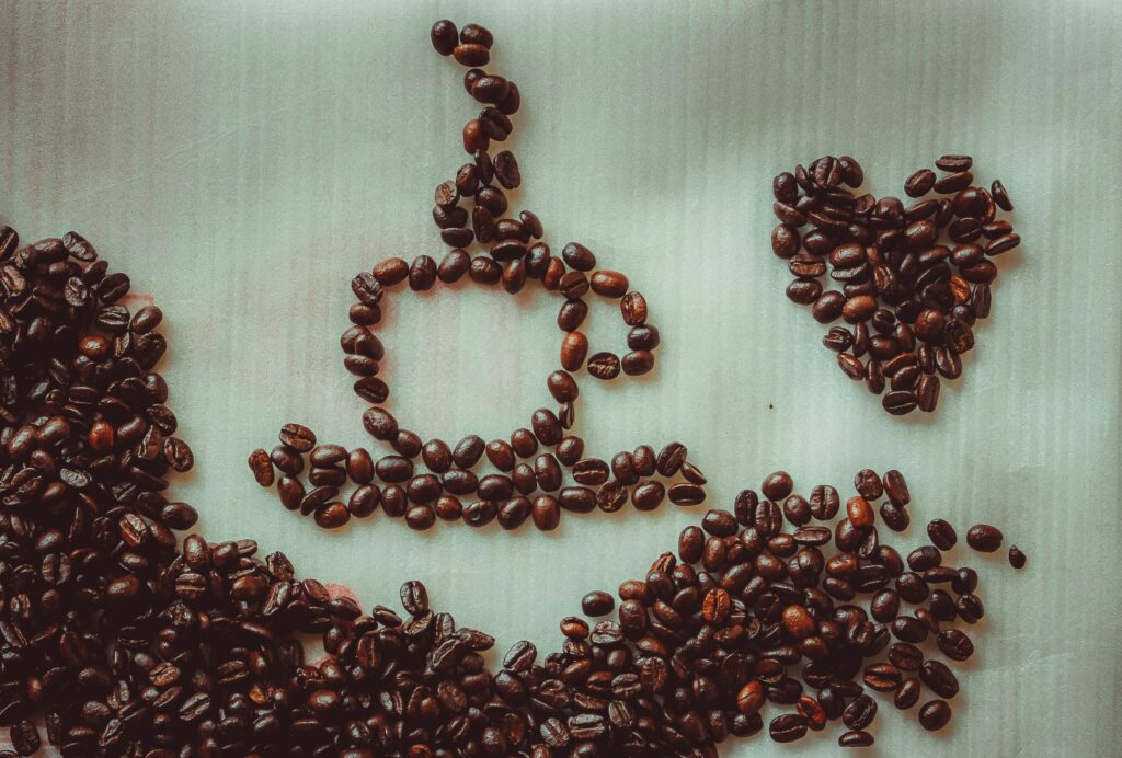 Coffee beans arranged into a cup and heart shape on a textured backdrop.